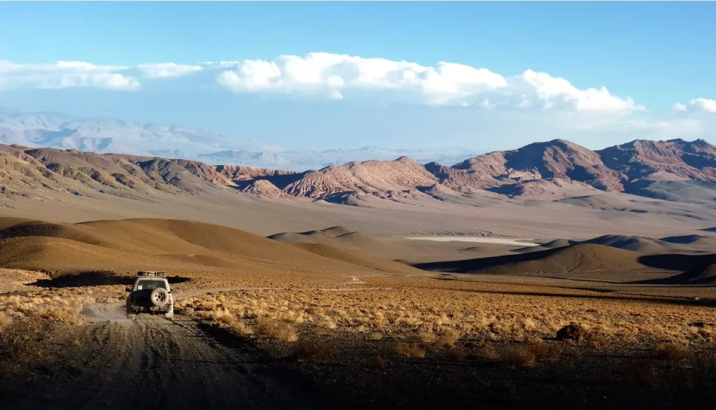 Carro 4x4 em uma estrada de terra atravessando as paisagens áridas e montanhosas do Deserto do Atacama.