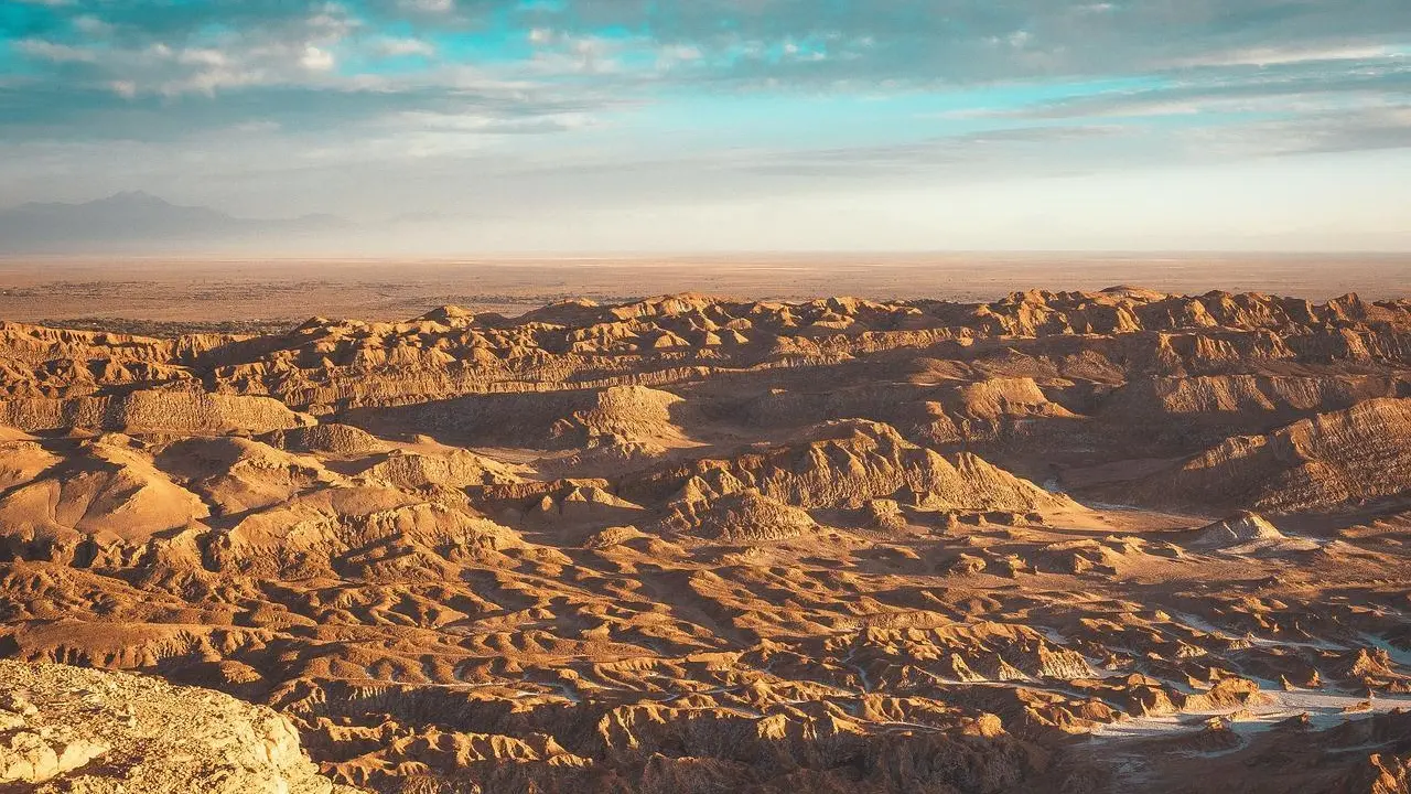 Vista panorâmica do Valle de la Luna no Deserto do Atacama, com formações rochosas esculpidas pela erosão, criando uma paisagem árida e deslumbrante sob um céu parcialmente nublado.