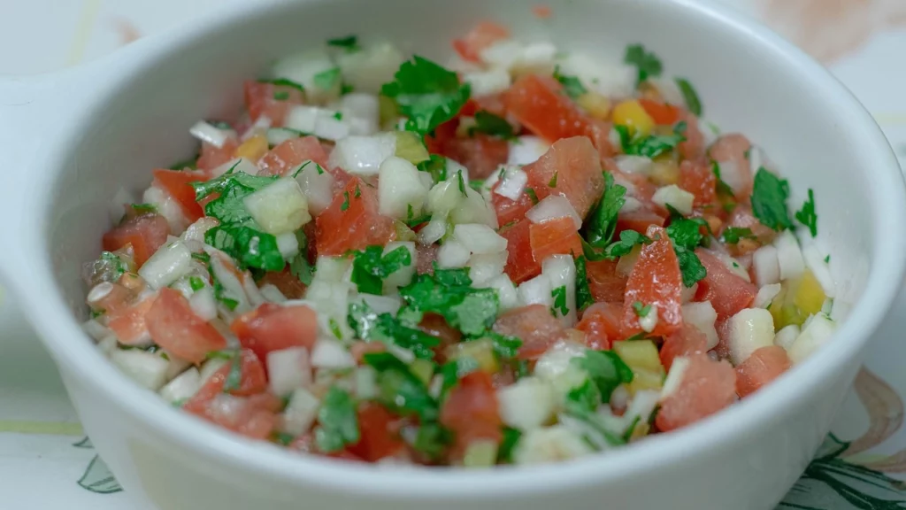 Porção de pebre chileno, um molho fresco de tomate, cebola, coentro e pimentão, perfeito para acompanhar diversos pratos típicos.