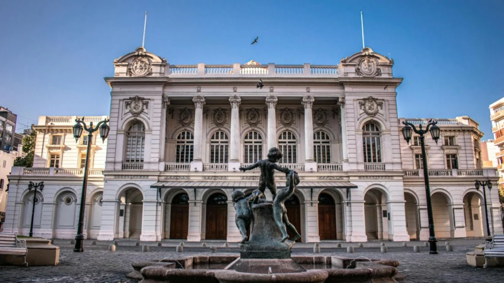 Prédio histórico branco com arquitetura clássica em Santiago, Chile, com uma fonte de estátua de crianças em primeiro plano.