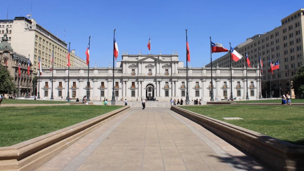 Palácio de La Moneda em Santiago, Chile, com bandeiras chilenas e uma ampla esplanada verde em frente ao edifício.